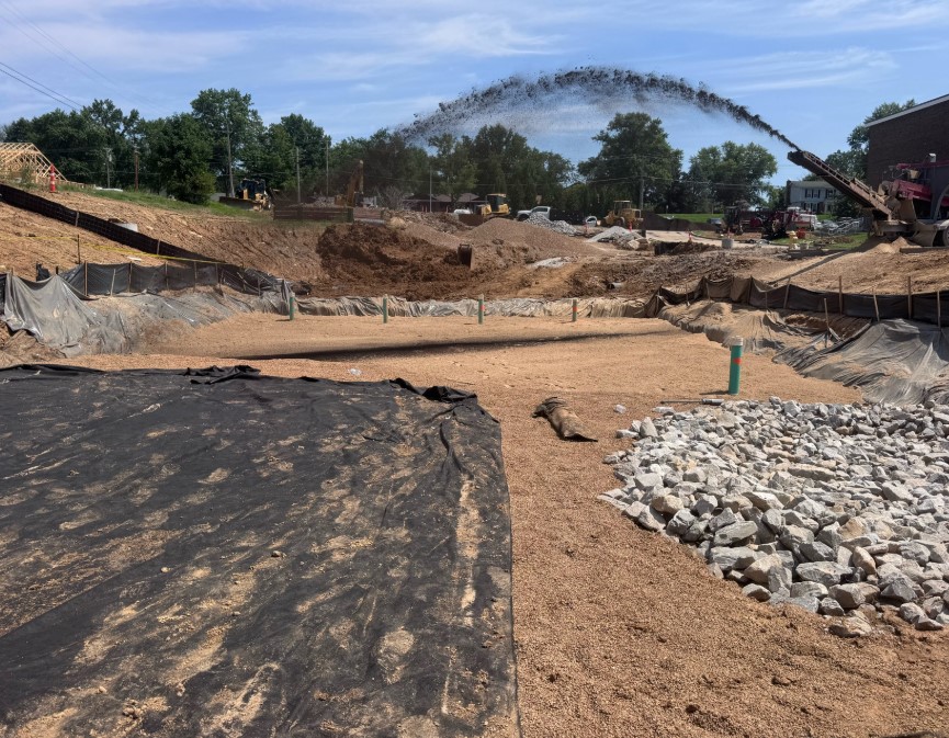 Kuesel crew rebuilding a bio retention basin in the St. Louis metro — new underdrain risers, filter fabric, sand filter media, and riprap outfall with a hydrovac discharging spoils