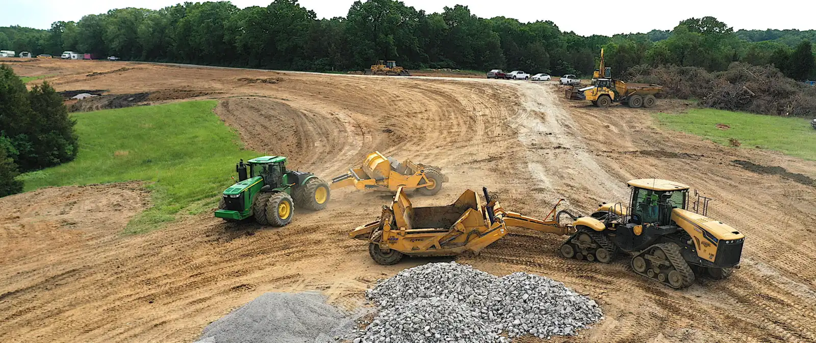 Scraper pans pulled by track tractors cutting a building pad at golden hour
