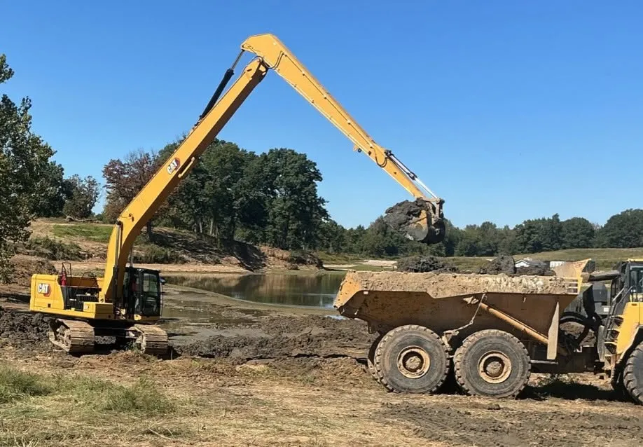 Long-reach excavator cleaning out a pond with an articulated truck